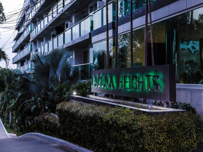 Laguna Heights main entrance sign with illuminated green letters, surrounded by dark green hedges at dusk.