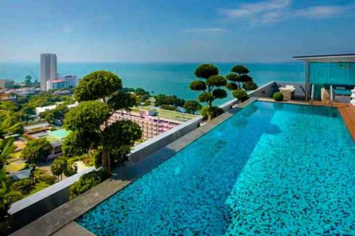 One Tower Pratumnak rooftop infinity pool overlooking the city skyline and ocean under a clear blue sky.