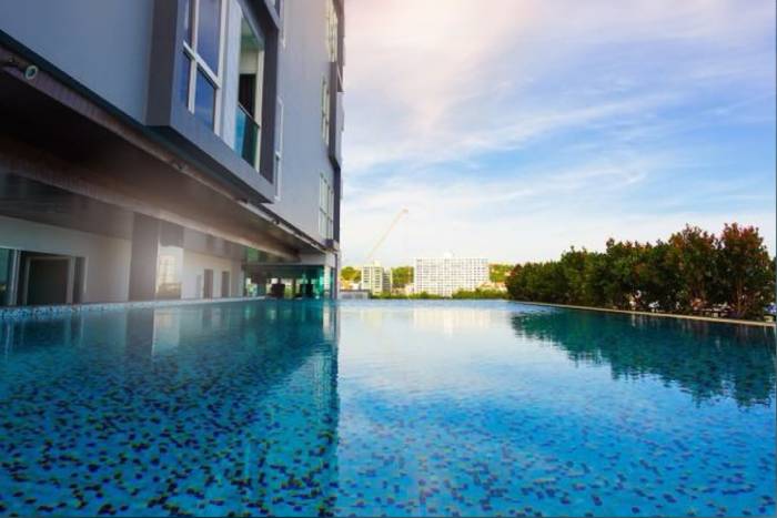 One Tower Pratumnak ground level swimming pool reflecting the building and blue sky, with surrounding trees.