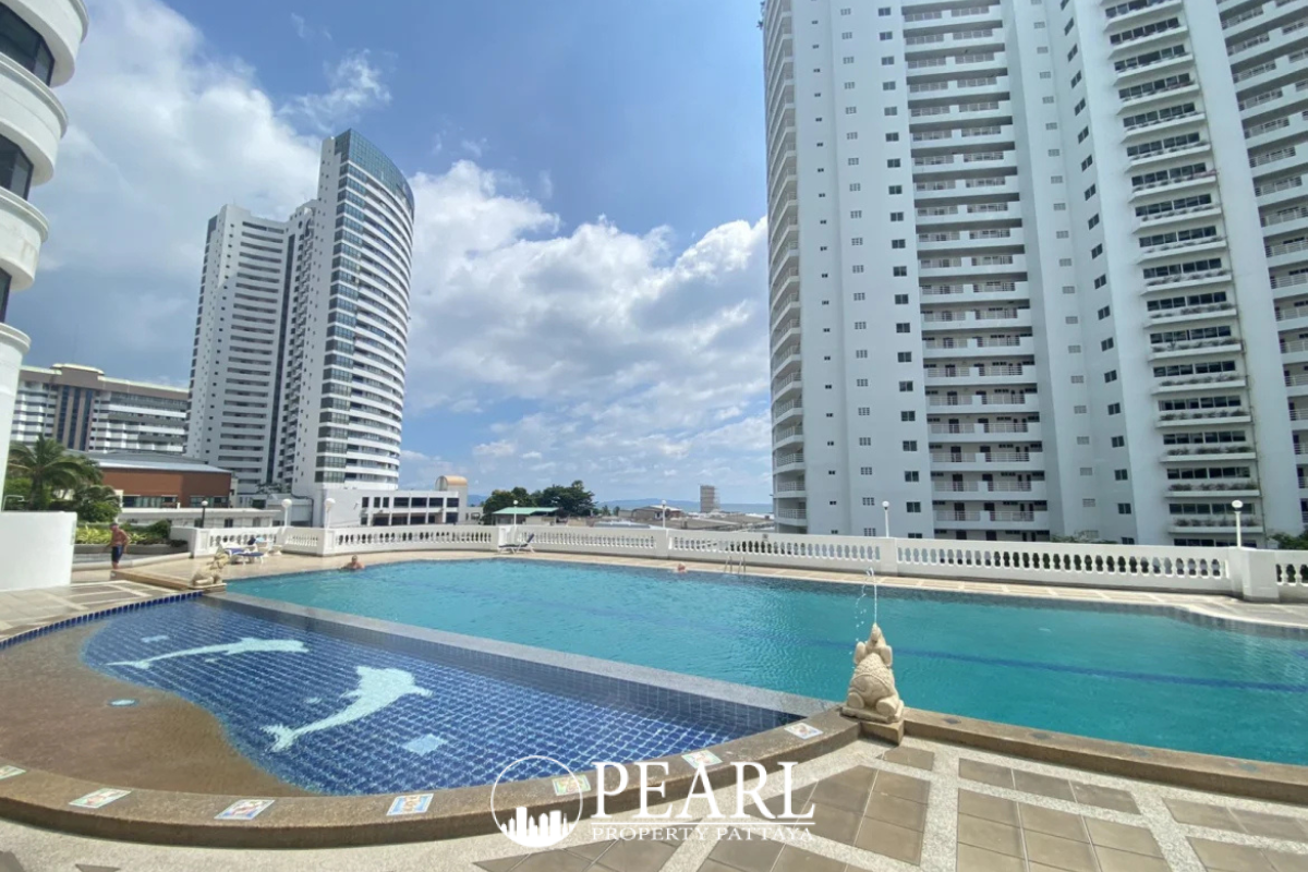 Jomtien Complex: Outdoor swimming pool with a covered seating area and white columns between two condo buildings.