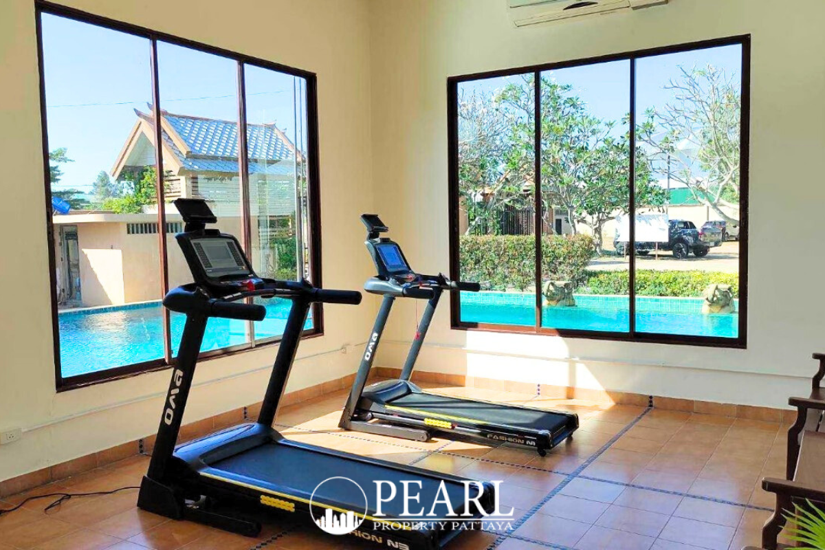 Nibbana Shade indoor gym with two treadmills facing large windows overlooking a swimming pool.