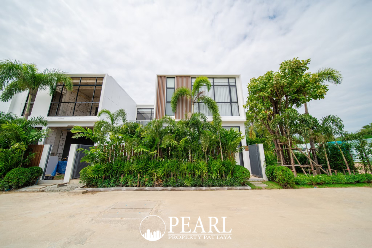 Maxx Pattaya modern white villas with large windows, surrounded by lush green tropical landscaping and palm trees.