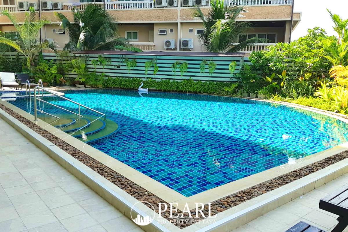 The Club House main entrance of a white multi-story building with green foliage, featuring balconies and a prominent sign.