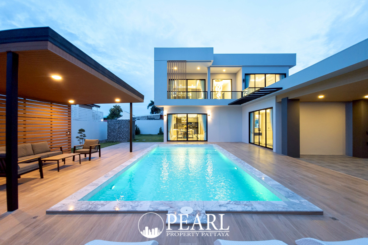 Eakmongkol Thepprasit modern two-story villa with a swimming pool and outdoor lounge chairs at dusk.