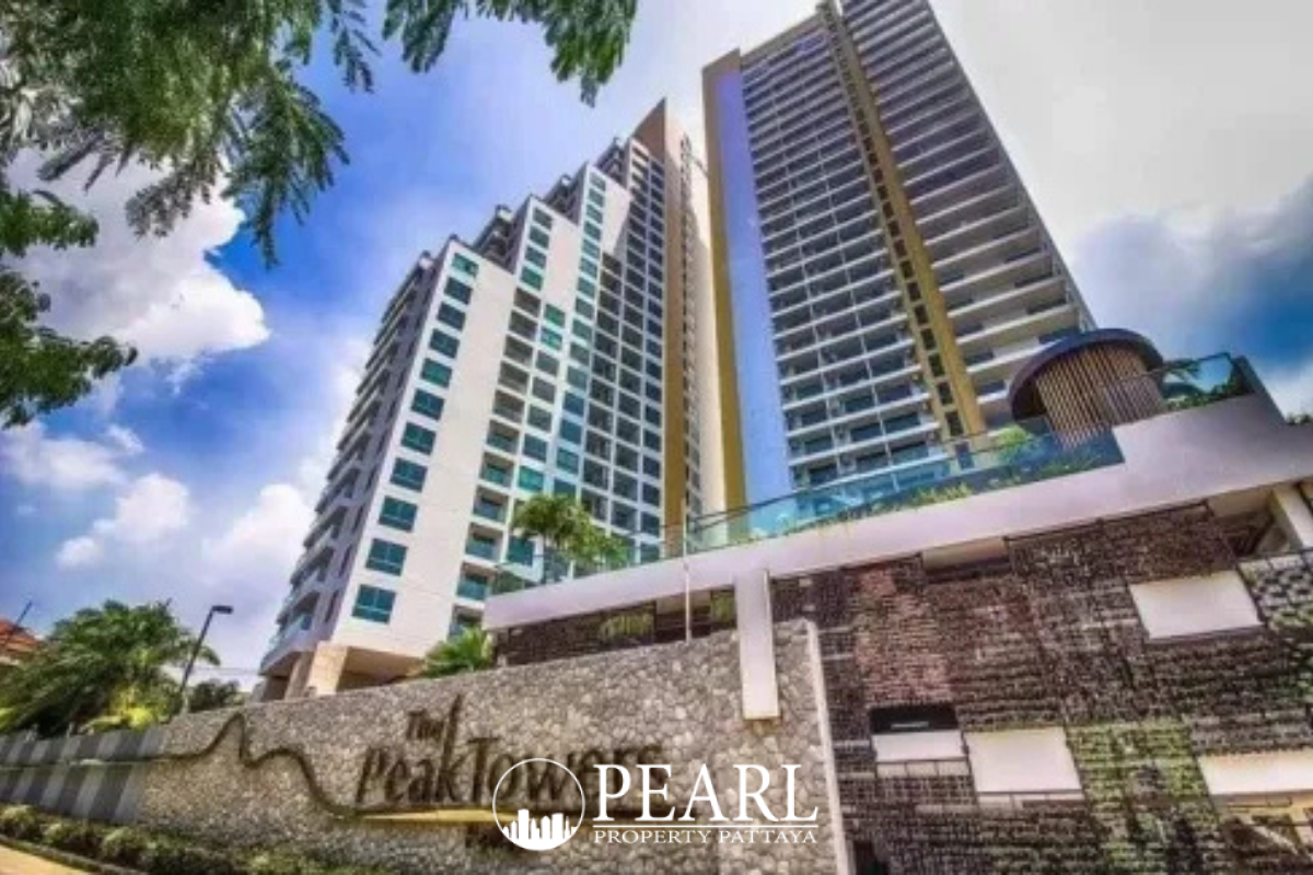 The Peak Towers high-rise condominium building with multiple balconies, surrounded by green trees, overlooking the ocean.